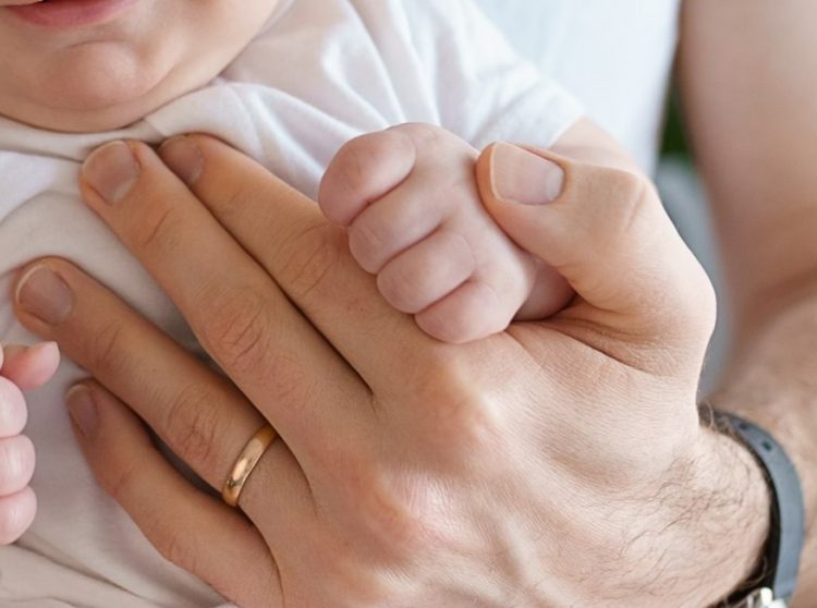 Close up photo of a dad holding a baby's hand